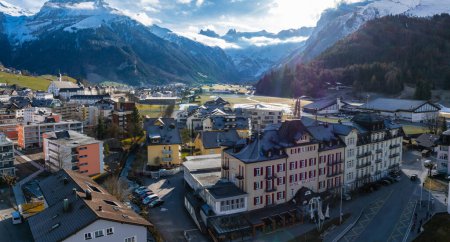 Photo for Panoramic daylight view of Engelberg, Switzerland, showcasing diverse architecture, the Hotel Bellevue, and clean streets. Snowcapped mountains and a valley hint at seasonal transition. - Royalty Free Image