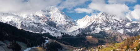 Téléchargez les photos : Vue panoramique d'Engelberg dans les Alpes suisses, avec des sommets enneigés, une zone boisée et le village à l'architecture alpine traditionnelle dans un cadre montagneux serein. - en image libre de droit