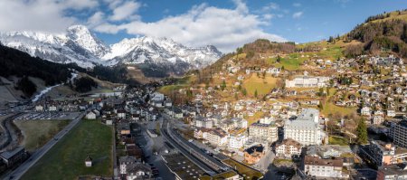 Panoramic view of Engelberg, Switzerland, showcasing its alpine village, green fields, accessible roads, and snowcapped mountains, highlighting the areas natural beauty and recreational appeal.