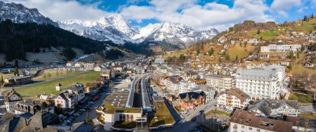 Photo for Panoramic view of Engelberg, Switzerland, showing a town with traditional architecture and a greendomed luxury hotel, surrounded by snowcapped Alps and clear skies. - Royalty Free Image