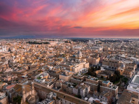 Une vue aérienne de Rome au crépuscule révèle un ciel passant du rose au bleu, avec la ville en lumière dorée. Bâtiments et rues clés mettent en valeur sa riche histoire et sa variété architecturale.