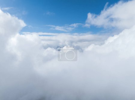 Luftaufnahme dichter, weißer Wolken, die Verbier in der Schweiz bedecken, mit klarem blauem Himmel darüber, was auf Höhenlage und Schönwetter hindeutet. Details von Stadt und Landschaft werden verschleiert.