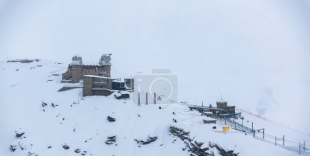 Téléchargez les photos : Un Zermatt enneigé, Suisse d'en haut, avec un chalet de montagne à gauche, des supports de téléski à droite, et des voies ferrées devant sous un ciel brumeux, montrant la scène de ski alpin sereine. - en image libre de droit