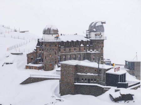 Ein großes Steingebäude mit Kuppeln, wahrscheinlich im Schweizer Skigebiet Zermatt, liegt im Schnee. Es ist von Skipisten und Liften umgeben und bietet eine ruhige, isolierte Atmosphäre, gebaut für strenge Winter.