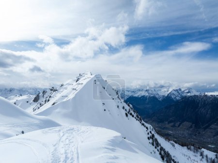 Foto de Una vista aérea de la estación de esquí de Verbier en Suiza muestra picos cubiertos de nieve con pistas de esquí, terreno accidentado y montañas dramáticas bajo un cielo parcialmente nublado.. - Imagen libre de derechos