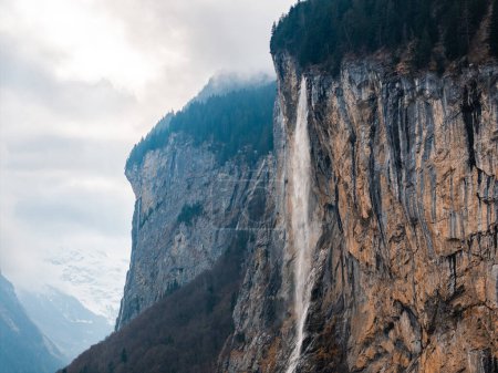 Ein atemberaubender Wasserfall fließt eine steile Klippe hinunter in Murren, den schroffen Bergen der Schweiz. Nebel verleiht der ruhigen, im Morgengrauen erleuchteten Szenerie ohne Menschen eine ätherische Note.