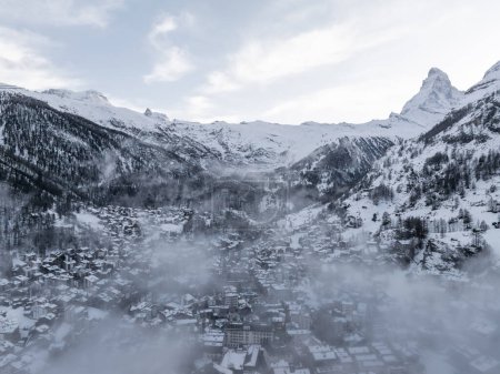 Téléchargez les photos : Vue aérienne de Zermatt, Suisse, montre une scène d'hiver sereine avec la ville parmi les montagnes enneigées et le Cervin emblématique. Mist ajoute une touche mystique, attirant les amateurs de sports d'hiver. - en image libre de droit