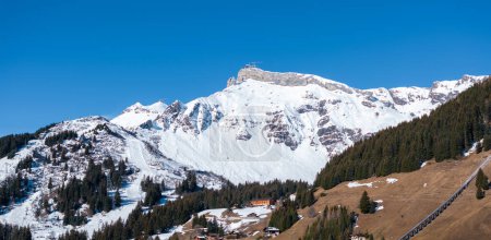 Luftaufnahme von Murren, Schweiz, zeigt Chalet-Gebäude gegen Schneegipfel. An einem sonnigen Tag aufgenommen, unterstreicht es die ruhige Stadt und die alpine Landschaft, wahrscheinlich im späten Frühling oder frühen Herbst.
