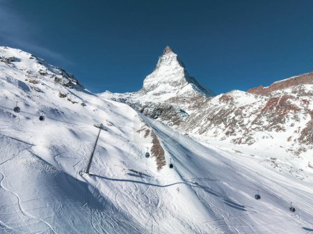 Eine Luftaufnahme von Zermatt, Schweiz, zeigt das Matterhorn und Skipisten mit Seilbahnen. Blauer Himmel und frische Loipen unterstreichen den Wintersport-Reiz.
