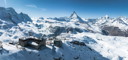 An aerial view of Zermatt ski resort in the Swiss Alps shows the Matterhorn, snow covered slopes, and alpine buildings. Skiers highlight its winter sports appeal.
