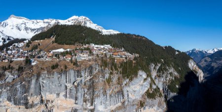 Photo for Aerial shot of serene Murren, Switzerland, with its alpine architecture among snow capped peaks, dense forests, on a cliffs edge facing the rugged Swiss Alps. - Royalty Free Image