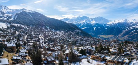 Photo for Aerial shot of Verbier, a Swiss Alps ski town, displays chalets in a snowy setting. It shifts through seasons under a clear sky, with grand mountains behind. Perfect for winter sports fans. - Royalty Free Image
