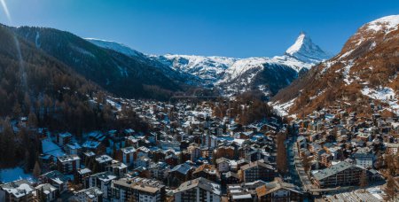 Photo for Aerial shot of Zermatt, a tranquil Swiss Alps ski resort, displays chalets and modern facilities under snow. The Matterhorn and snow capped peaks loom behind, creating a serene, majestic winter haven. - Royalty Free Image