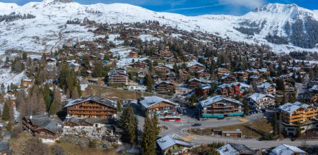Verbier, Schweiz, von oben betrachtet, zeigt eine Skistadt in verschneiten Bergen. Hier mischen sich Kiefern, Schnee und Almhütten. Eine Straße mit rotem Bus verleiht dem Skigebiet ein einladendes Flair.
