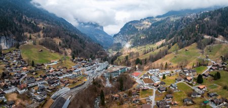 Vue aérienne de Murren, en Suisse, mettant en valeur l'architecture alpine traditionnelle au milieu de prairies luxuriantes et de montagnes escarpées. Une route sinueuse suggère l'accessibilité à cette vallée tranquille et isolée.