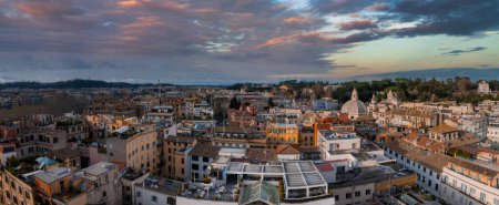 An aerial view of Rome at dusk reveals dense, warm toned buildings, historic domes, and spires. Aerial panoramic cityscape of Rome, Italy, Europe. Roma is the capital of Italy. 