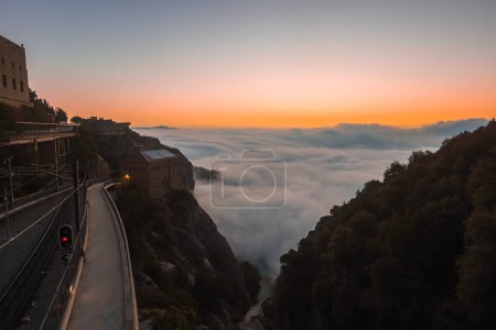 Vue aube ou crépuscule d'un chemin de fer tournant autour d'une montagne avec un feu rouge, surplombant une vallée nuageuse près de Barcelone, peut-être Montserrat.