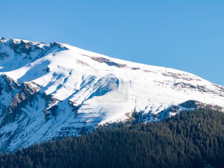 Photo for A snow capped mountain in Murren, Switzerland, under a clear sky, has steep slopes with snow and rock. Higher areas are snowier, and lower ones lead to dense forests. - Royalty Free Image