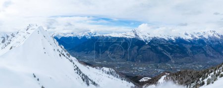 Téléchargez les photos : Un plan aérien montre Verbier, un paysage enneigé de Suisse, des pistes de ski, un pic et les Alpes sous un ciel partiellement nuageux. Son charme hivernal est dans la neige intacte et de douces ombres nuageuses. - en image libre de droit
