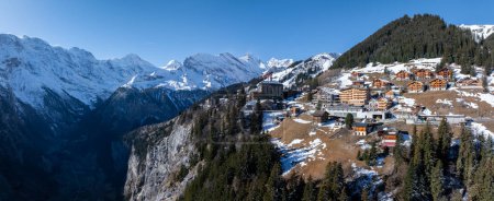 Photo for Aerial view of Murren, Switzerland, showcases a serene mountain village with traditional chalet style buildings on a cliff. Snow covered Swiss Alps and clear skies create a picturesque backdrop. - Royalty Free Image