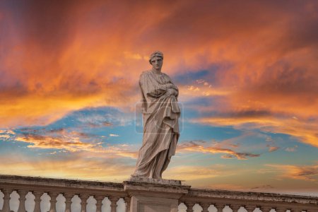 Eine klassische Marmorstatue mit drapiertem Gewand steht unter dem pulsierenden Himmel bei Sonnenuntergang im Vatikan. Heitere Schönheit von Kunst und Architektur in diesem eleganten Bild eingefangen.