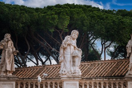 Klassische Statuen auf einem Gebäude in der Vatikanstadt. Verwittert, im Renaissance- oder Barockstil gemeißelt. Kiefernkulisse, moderne Überwachungskamera, die Geschichte mit Technologie verbindet.
