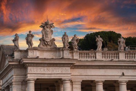 Atemberaubender Blick auf klassische Statuen und Architektur im Vatikan. Statuen auf Brüstung, zentrale Skulptur mit päpstlichen Symbolen, Hausfassade mit Inschriften und dramatischem Sonnenuntergang sky.uul