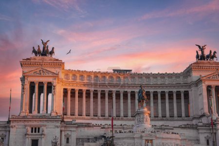 Una majestuosa vista de Altare della Patria, o Monumento Nacional a Víctor Manuel II, en Roma, Italia. Fachada de mármol blanco, estatuas y bandera italiana bajo un cielo azul claro.