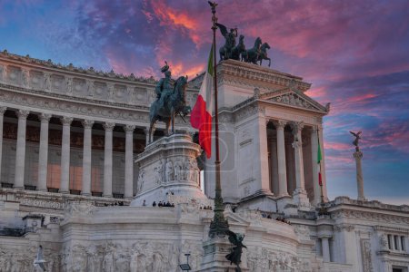 Monumento Nacional Víctor Manuel II en Roma, Italia, bañado por la suave luz del sol. Bandera de Italia en primer plano, estatuas, columnas, turistas, cielo despejado, hora dorada.