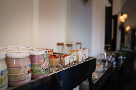 Foto de Una lujosa selección de desayuno en un hotel de Roma. Envases de yogur de bio yogur orgánico, copas de vidrio de parfait con fresas, fondo buffet elegante. - Imagen libre de derechos