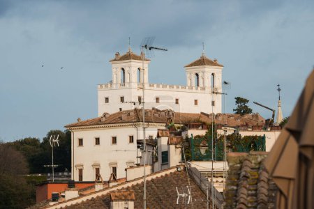 Historisches Gebäude mit weißer Fassade, Türmen, kleinen Kuppeln, Kreuzen in Rom. Dächer, Antennen, Grün verschmelzen mit Alt und Moderne..