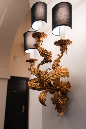 Lámpara de pared de lujo con acabado dorado, similar a una rama con hojas o pétalos, en un hotel de Roma. Decoración elegante con ambiente de iluminación cálida.