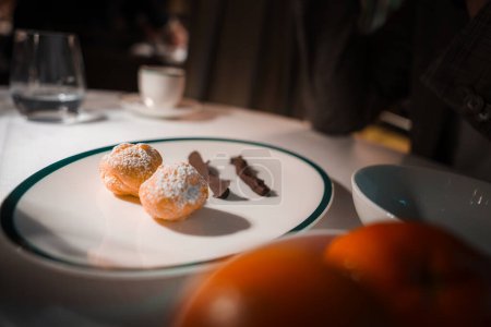 Téléchargez les photos : Vue rapprochée d'une assiette à dessert blanche avec bordure verte, contenant deux pâtisseries saupoudrées de sucre et de garnitures au chocolat dans un cadre de restaurant haut de gamme. - en image libre de droit