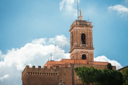 Historic brick tower rising above a fortified building, possibly a bell tower or part of a religious structure. European architecture, could be in Italy.