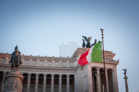 View Altare della Patria in Rome, Italy. Daytime shot with the national flag and equestrian statue. Monument features intricate details, symbolic statues, and historical significance.