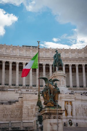 Drapeau italien sur un mât de drapeau avec statue équestre en bronze et grand bâtiment classique en arrière-plan. Probablement en Italie, peut-être à Rome, avec une signification historique importante.