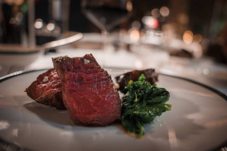 Luxuriöses Restaurant mit Nahsicht auf ein mittelseltenes Steak, garniert mit grobem Salz und grünem Gemüse. Anspruchsvolles Ambiente.