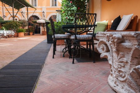 Luxury hotel outdoor seating area in Rome with terracotta flooring, pastel walls, elegant chairs, lush greenery, and tranquil ambiance for relaxation.