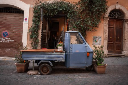 Charming urban scene in Italy with an Ape truck parked on cobblestone street. Detailed architectural elements, shops, and signage add picturesque charm.