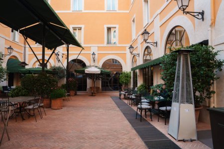 Innenhof des Luxushotels in Rom mit warmer orangefarbener Architektur, Terrakottafliesen, viel Grün und Außengastronomie für die Gäste. Ruhiges und elegantes Ambiente.