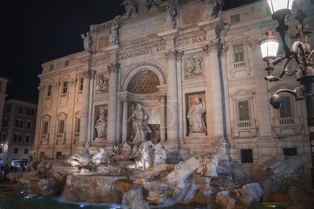 Famosa fuente barroca de Trevi en Roma, Italia iluminada por la noche. Esculturas detalladas y arquitectura destacada por la iluminación artificial en un momento de serenidad.