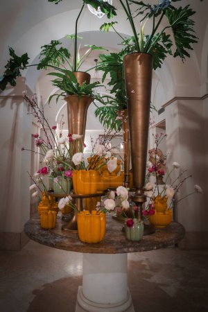 Luxuriöses Blumengesteck auf rundem Marmortisch in elegantem Restaurant-Ambiente. Gold-, Gelb- und Metallic-Akzente verleihen dem anspruchsvollen Interieur Opulenz.