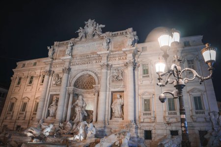 Trevi Fountain in Rome, Italy, illuminated at night. Features sculptures of Oceanus, Abundance, Salubrity, horses, and tritons. Popular tourist destination for good luck coin toss.