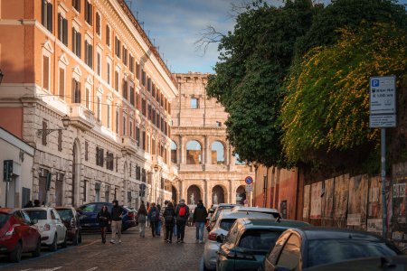 Téléchargez les photos : Scène de rue européenne en fin d'après-midi à Rome, Italie. Architecture classique, y compris le Colisée en arrière-plan, les voitures stationnées, les piétons et un panneau de signalisation. - en image libre de droit