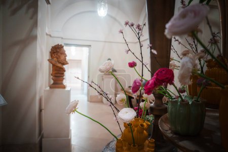 Elegantes Interieur mit lebendigem Blumenschmuck auf einem Tisch in luxuriösem Restaurant-Ambiente. Raffinierte Architektur, klassische Skulptur, sanft warmes Licht.