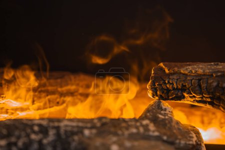 Lueur chaude de grumes brûlantes avec des bords carbonisés, des flammes vives dans des tons jaunes et orange sur un fond sombre, créant une atmosphère chaleureuse et accueillante. Gros plan de la cheminée ou du feu de camp.