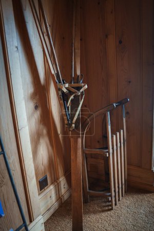 Photo for Room corner with wooden paneling, vintage skis, leather bindings and traditional sled in a cozy, rustic setting evoking winter nostalgia. Beige carpet on floor, no specific location indicated. - Royalty Free Image