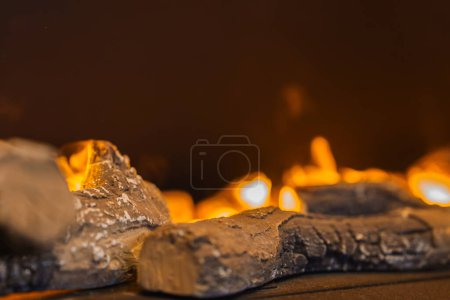Vue rapprochée d'une cheminée à gaz avec des grumes artificielles réalistes, des surfaces carbonisées et des détails en cendres blanches. Flammes chaudes en fonctionnement, créant une ambiance chaleureuse.
