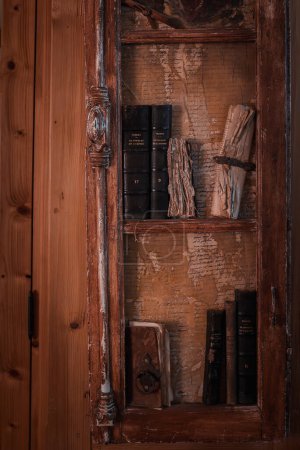 Rustykalna drewniana półka z klasycznym wyglądem, wbudowana w ścianę. Posiada ciemne, stare ramy drewniane z rzeźbami, stare książki, dokumenty i narzędzia wieku. Powoduje nostalgię i atmosferę historii.