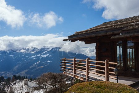 Rustikales Holzchalet mit Balkon mit Blick auf verschneite Gipfel in bergiger Region. Traditionelles Laternenlicht, heitere Atmosphäre. Idealer Rückzugsort in den Bergen.